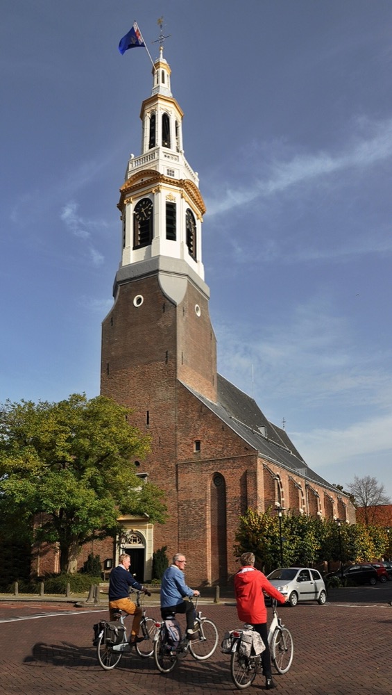 De Grote Kerk in Nijkerk met de vlag in top, fietsers op het plein ervoor